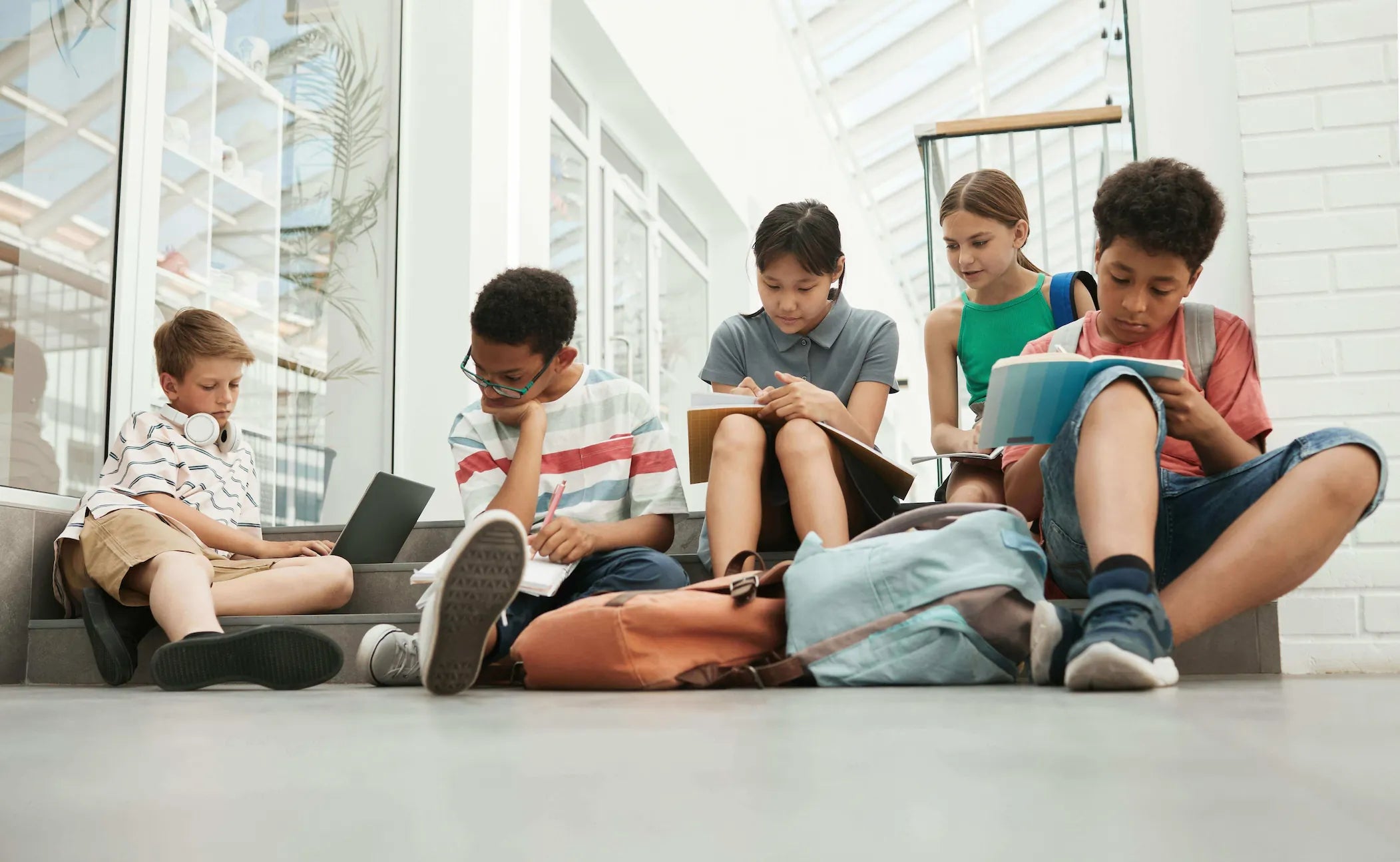 Vijf leerlingen studeren samen op de trappen van een modern gebouw met studiemateriaal.